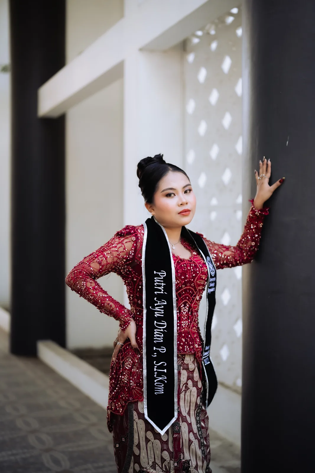 Putri Ayu Dian P berpose mengenakan busana merah dan selempang.